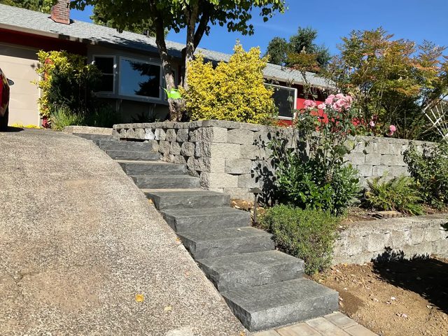 Basalt block staircase climbing from the driveway beside a block retaining wall